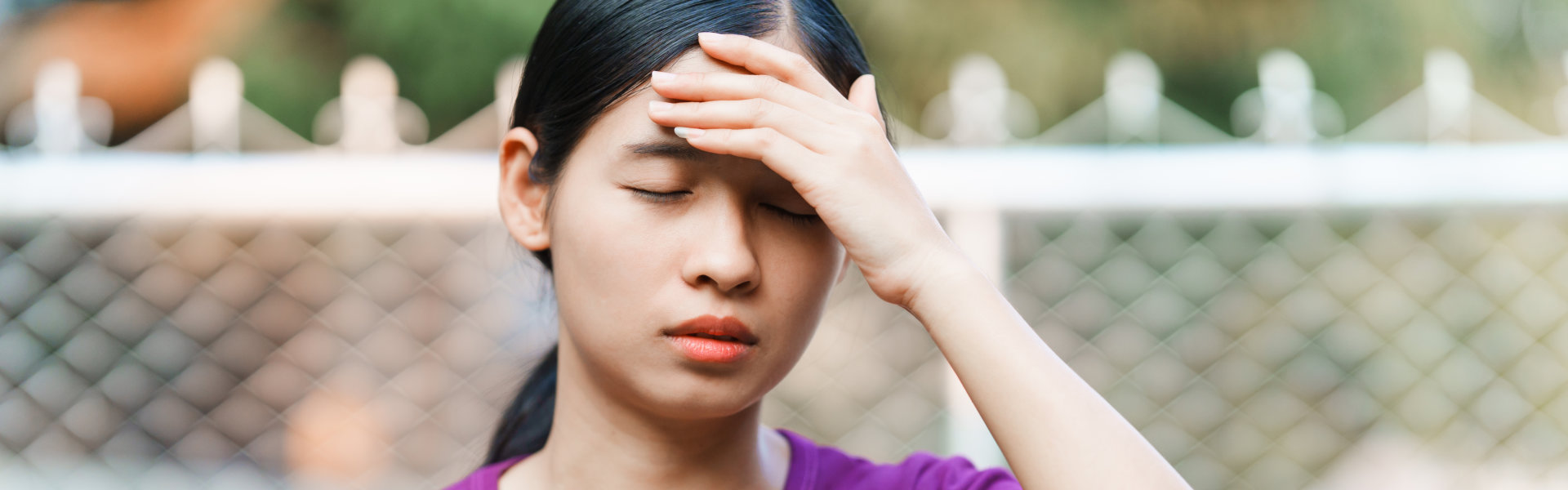 Woman Holding Forehead with Painful Expression Outdoors